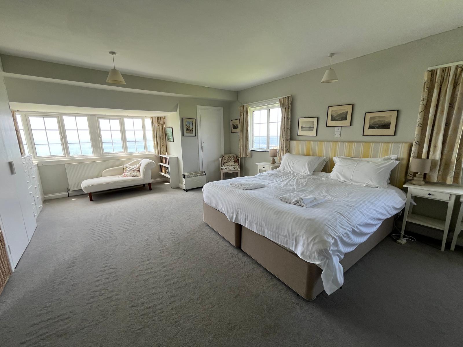 A spacious sea-facing bedroom at Westwinds with a king bed, chaise, and windows looking out to the Atlantic